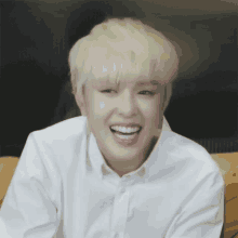 a young man with blonde hair and white shirt is smiling