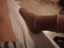 a person laying on a bed with a brown sock on their foot