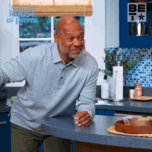 a man in a grey shirt is standing in a kitchen with the house of payne logo on the wall