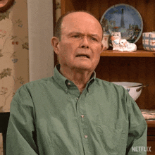 a man in a green shirt is sitting in front of a shelf with plates on it and a netflix logo