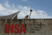 a person sitting on top of a concrete wall that says institut national des sciences appliques lyon