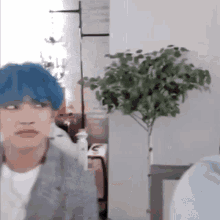 a man with blue hair is making a funny face in front of a plant .