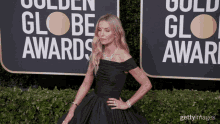 a woman in a black dress stands on a red carpet in front of a sign that says golden globe awards