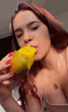 a woman with red hair is eating a mango with a gold necklace