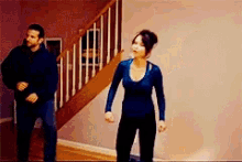 a man and a woman are dancing in a living room in front of a staircase