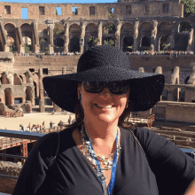 a woman wearing a black hat and sunglasses smiles in front of the colosseum in rome