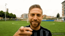 a man in a black and white striped shirt is pointing at the camera while standing on a soccer field