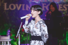 a woman singing into a microphone in front of a loving forest sign