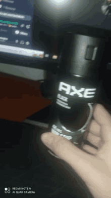 a person is holding a bottle of axe deodorant in front of a computer screen