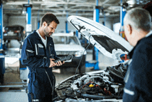 two men are working on a car in a garage with the hood up