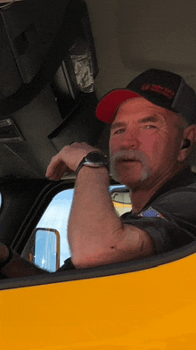 a man wearing a trucker hat is sitting in the driver 's seat of a vehicle