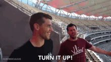 two men standing in a stadium with the words turn it up