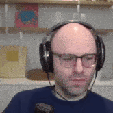 a bald man wearing glasses and headphones looks at the camera