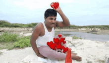 a man is sitting on a beach holding a heart in his hand .