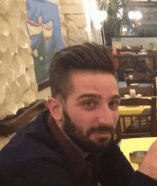 a man with a beard sits at a table in front of a painting