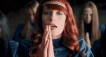 a woman with red hair is praying in front of a group of women in blue dresses .