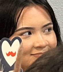 a woman is holding a heart with a moustache on it .