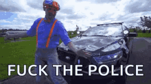 a man in a blue shirt and suspenders is standing in front of a police car and holding a gun .