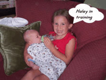 a little girl is holding a baby and a speech bubble says haley in training