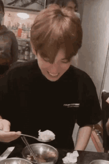 a young man in a black shirt is sitting at a table eating food .