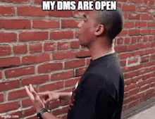 a man standing in front of a brick wall with the words my dms are open above him