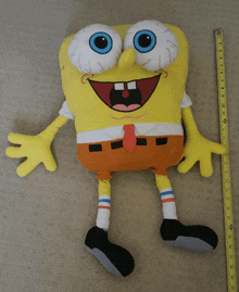 a stuffed spongebob with blue eyes is being measured by a yellow tape measure