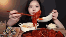 a woman is eating a meal with a spoon and chopsticks with a bowl of rice balls in the background