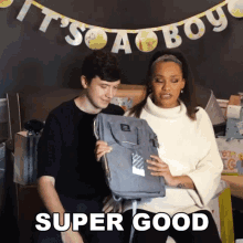 a man and a woman are sitting in front of a baby shower banner that says it 's a boy