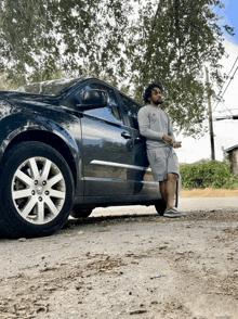 a man leans against a black car on the side of a road