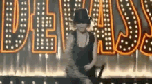 a woman in a hat is dancing on a stage in front of a neon sign that says vegas .