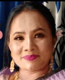 a close up of a woman 's face wearing a purple saree and gold earrings .