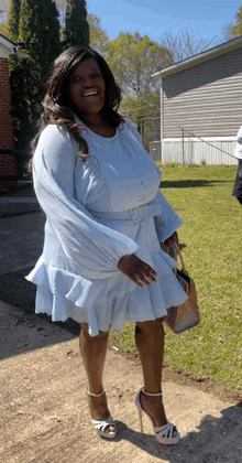 a woman in a light blue dress and heels is standing in front of a house