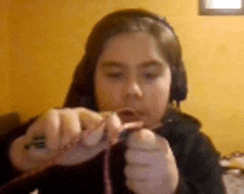 a young girl wearing headphones is crocheting a bracelet .