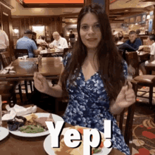 a woman in a blue dress is sitting at a table with a plate of food and the word yep on the plate