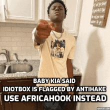 a young man is pointing at the camera in a kitchen while wearing an african hook shirt .