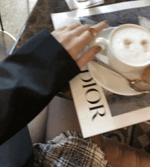 a person is holding a cup of coffee next to a magazine that says dior