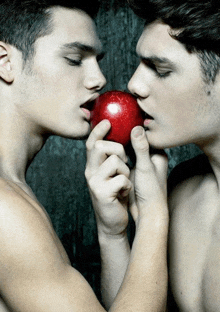 two men are kissing while one is holding an apple in his hand