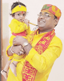 a man in a yellow shirt is holding a baby who is wearing a yellow headband and playing a flute