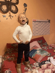 a little girl is standing on a bed with a 2022 calendar behind her