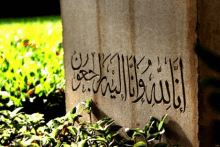 a stone with arabic writing on it surrounded by greenery