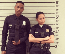 a man and a woman in police uniforms stand in front of a wall with measurements on it