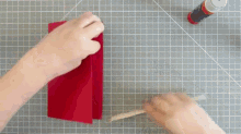 a person is holding a piece of red paper on a cutting board next to a stick of glue .