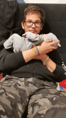 a man wearing glasses is holding a baby in his arms with a bracelet on his wrist that says i love you