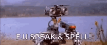 a robot is standing in a field next to a body of water and says `` fu speak & spell '' .