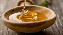 honey is pouring into a wooden bowl on a table .