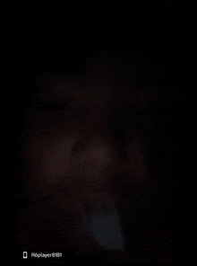 a close up of a person 's face in the dark with a cell phone in the background .