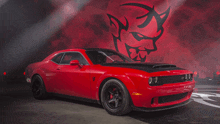 a red car is parked in front of a red background with a devil on it