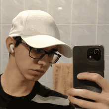 a man wearing glasses and a white hat takes a selfie with his phone