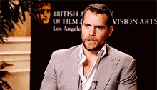 a man in a suit is sitting in front of a sign that says british academy of film and vision arts los angeles .