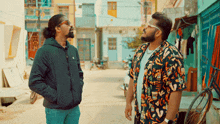 two men standing next to each other on a street with one wearing a hawaiian shirt